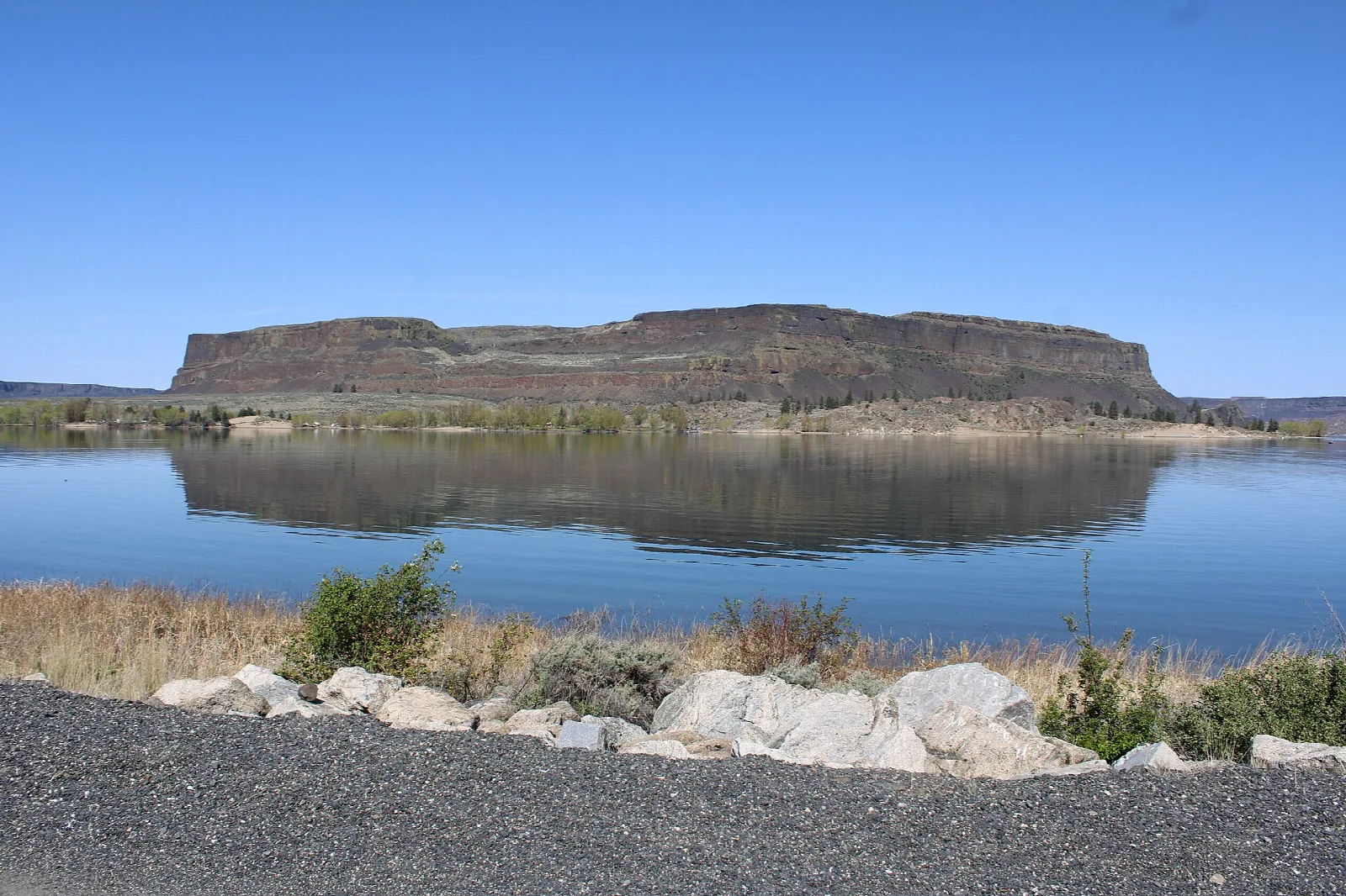 Steamboat Rock reflected in blue lake water beyond a rocky shore