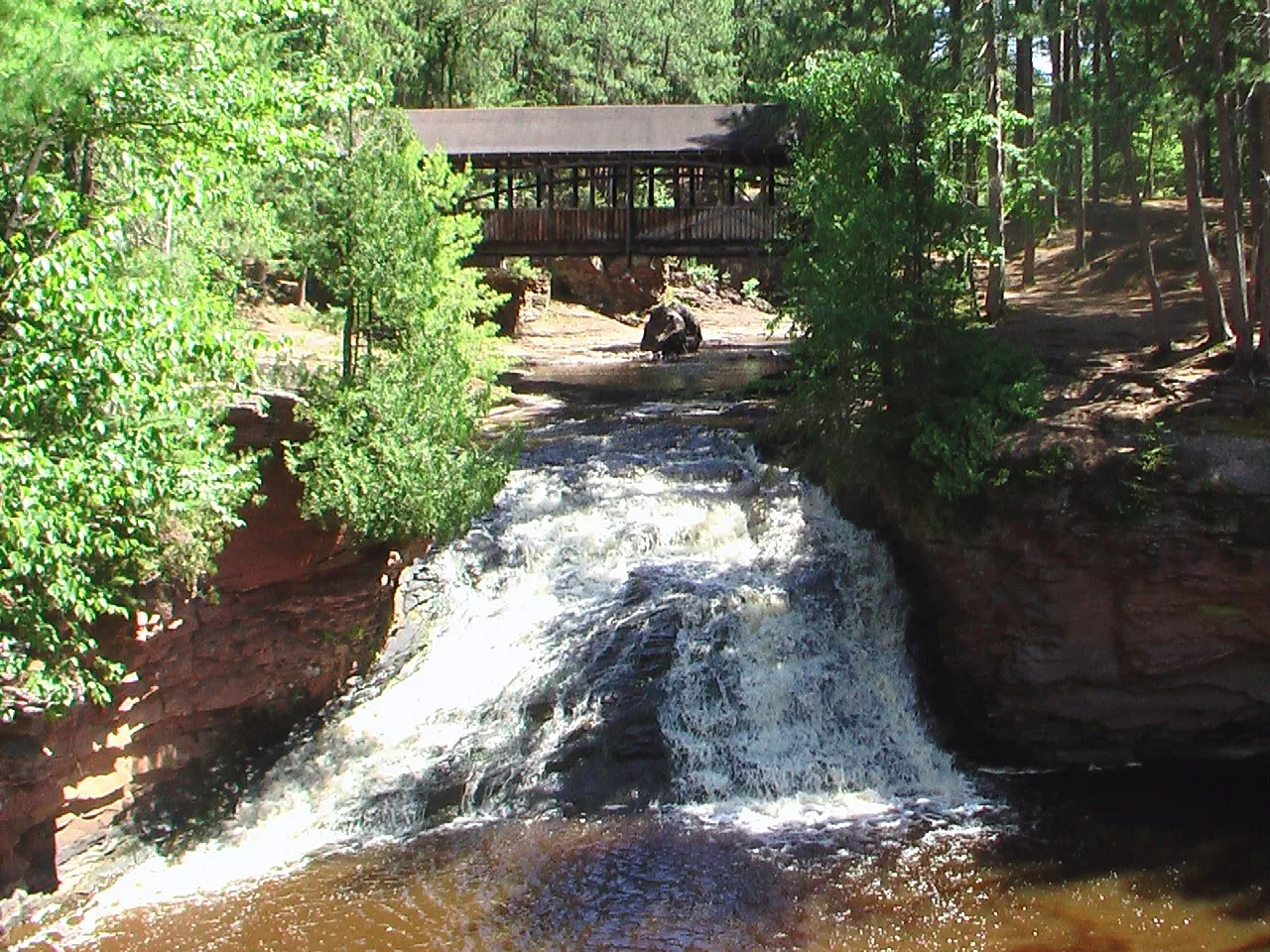 Waterfall tumbling over red rock with a covered bridge above