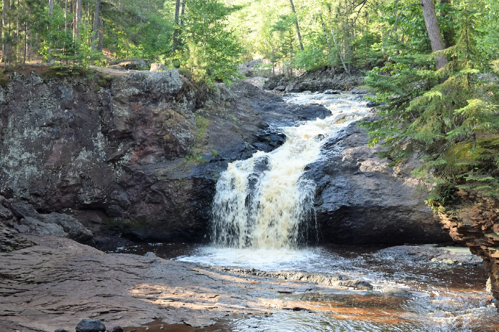 Small waterfall dropping over dark rock into a pool