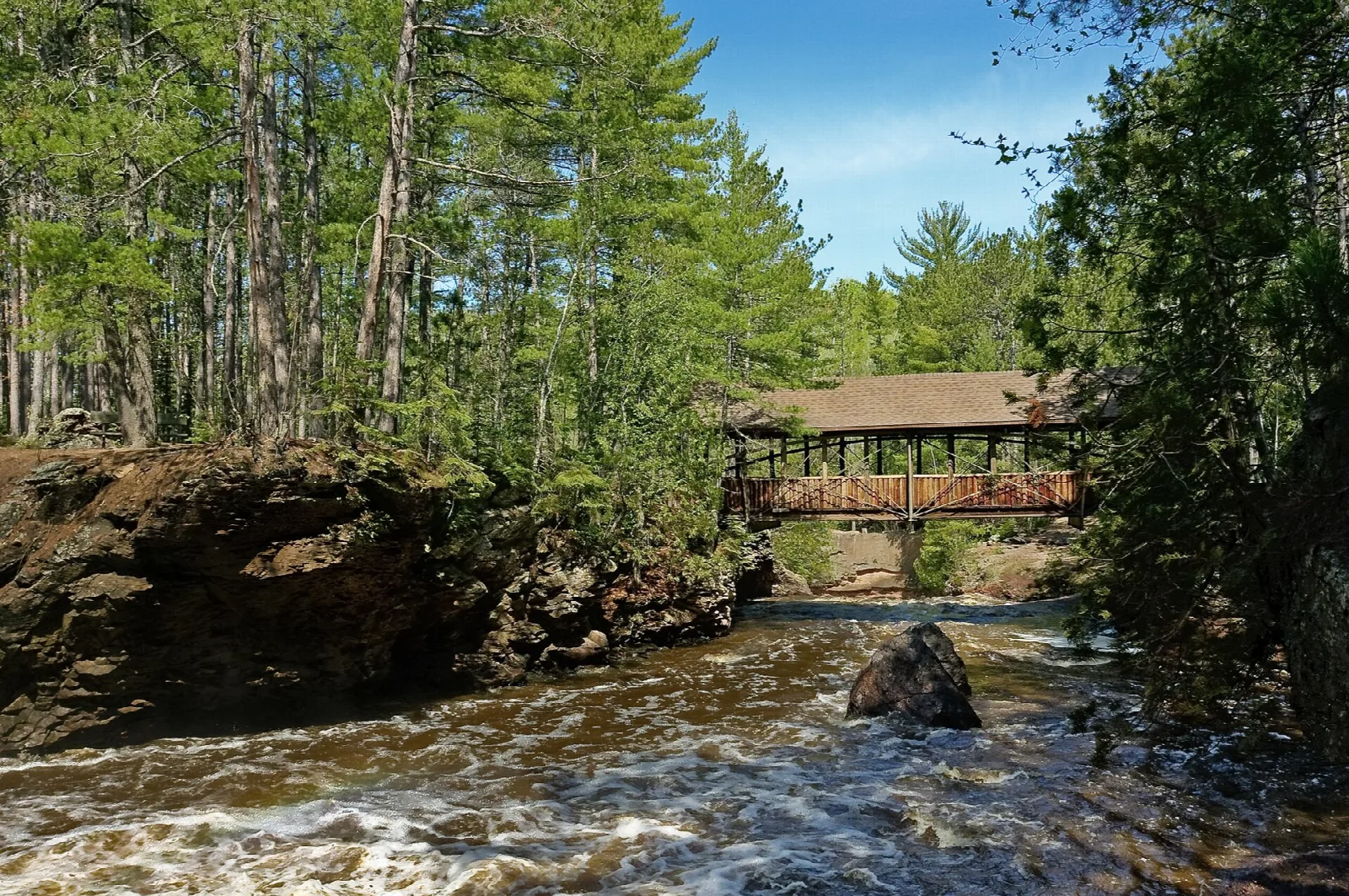 Wooden covered bridge over a rushing river among pine trees
