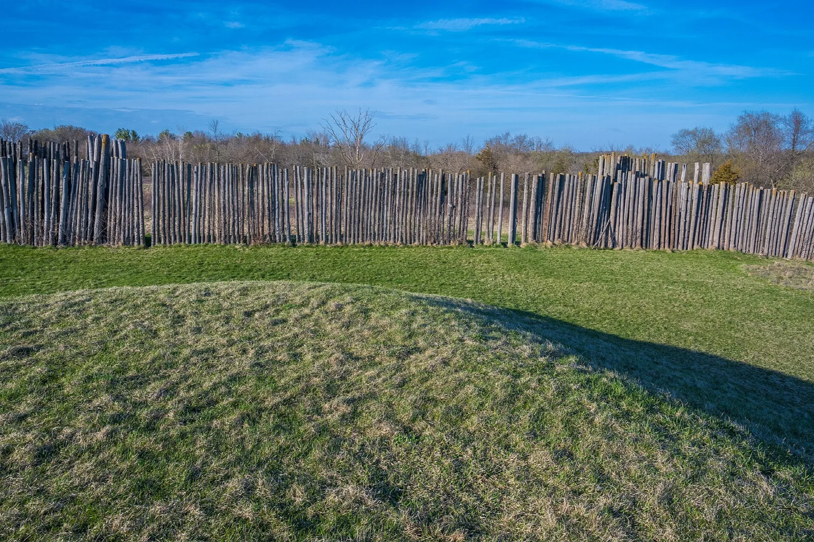 Wooden stockade fence behind a grassy mound under blue sky