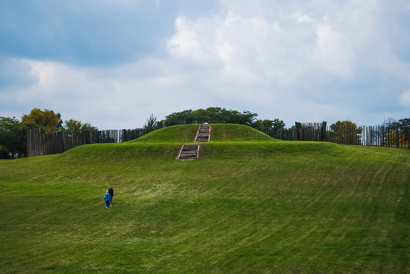 Grassy platform mound with steps and a wooden stockade behind it