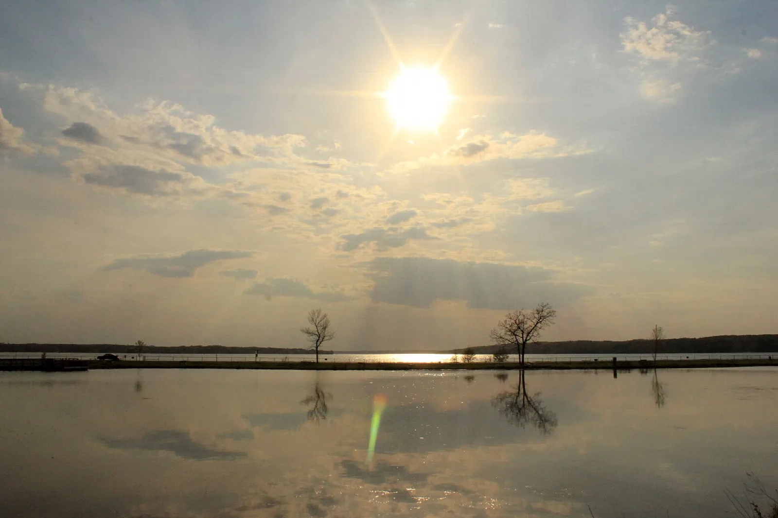 Sun low over a calm lake with reflections and distant trees