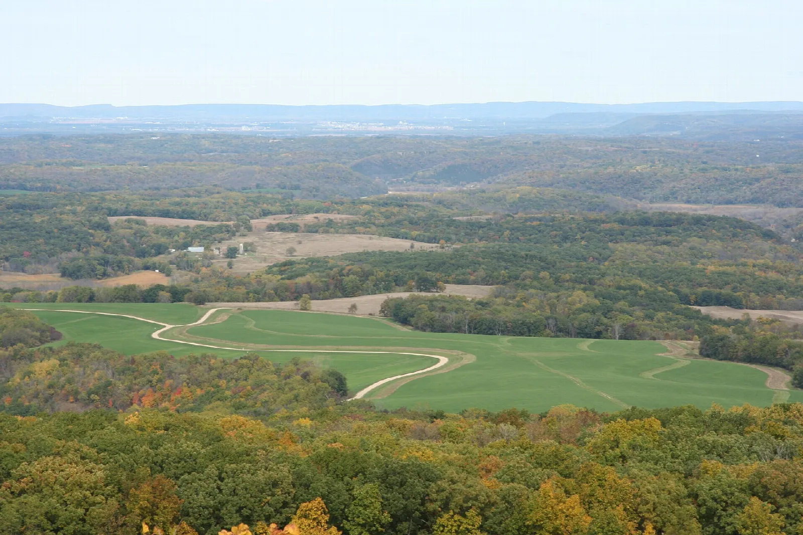Wide view over wooded hills and a green field with a winding path