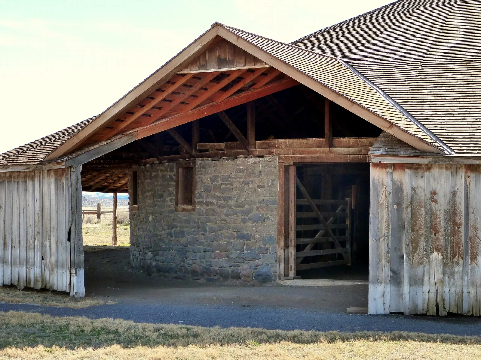 Barn entrance with stone walls, wood siding, and an open gabled roof