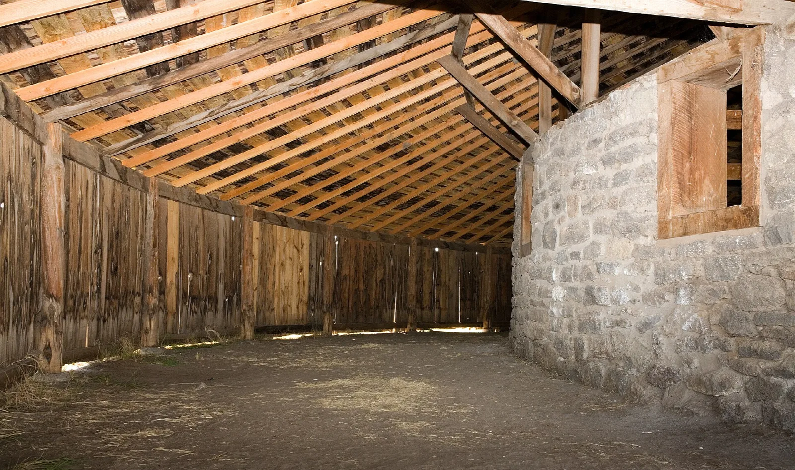 Curved barn interior with a rafter roof and stone wall