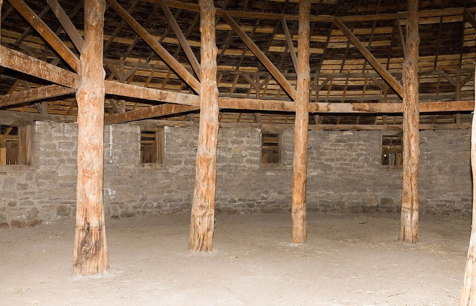 Inside the barn: wooden posts and rafters around a stone wall and dirt floor
