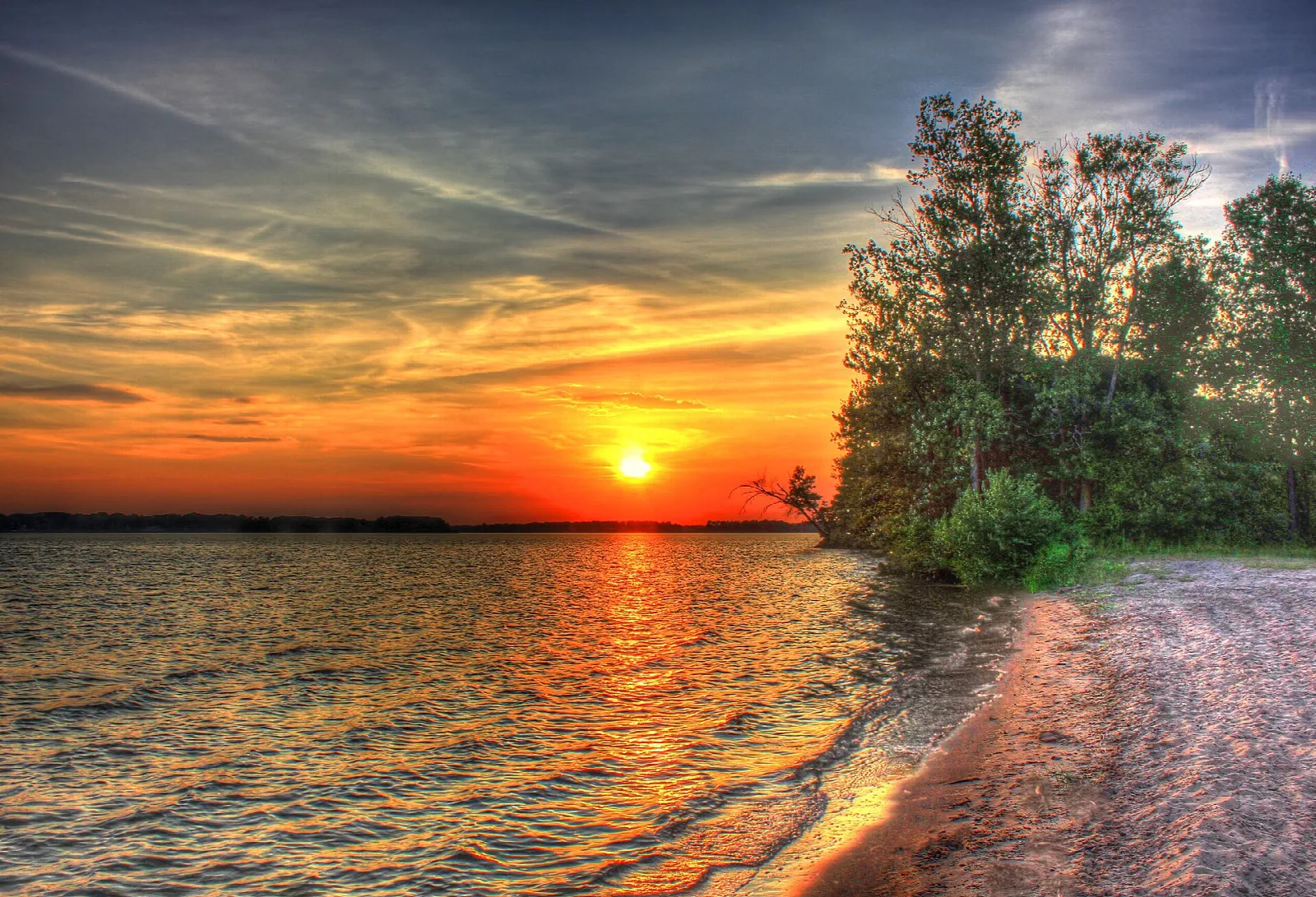 Orange sunset over a lake with a pink sandy shore and trees