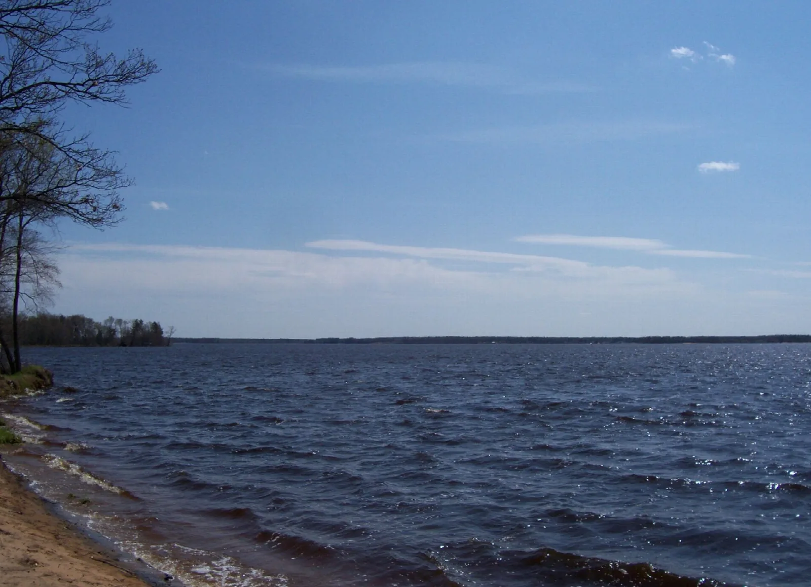 Wide blue river lake with a sandy shore and distant tree line
