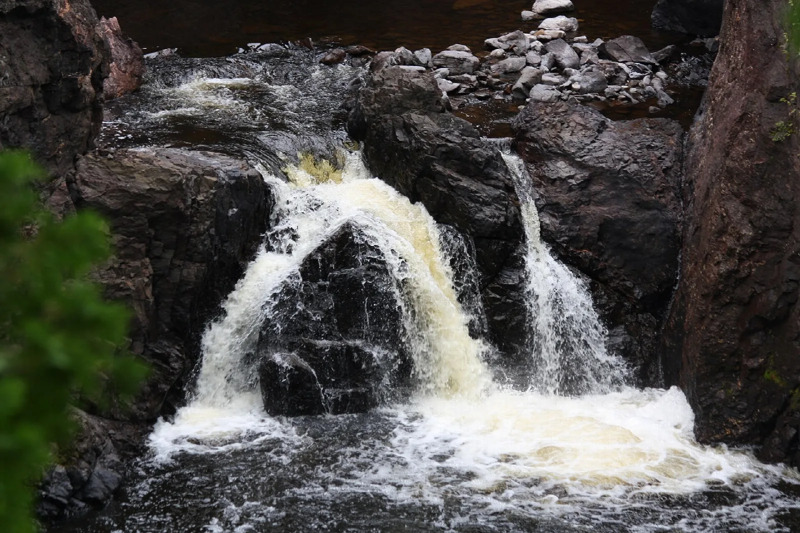 Waterfall splitting around dark rock into churning white water