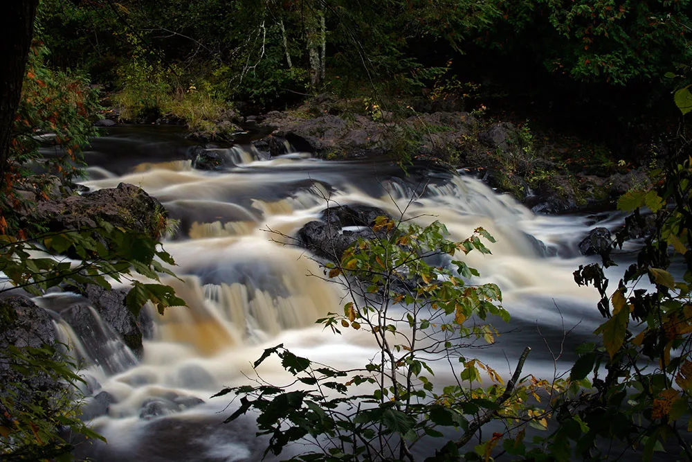 Long-exposure river cascading over rocks in shaded forest