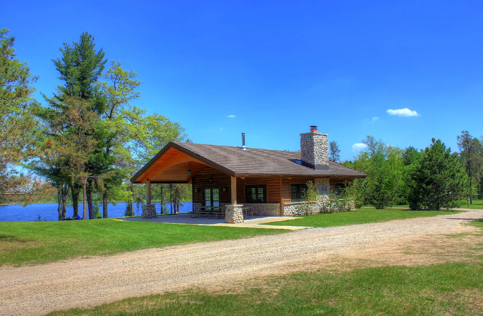 Wooden shelter with a stone chimney beside a lake and gravel road