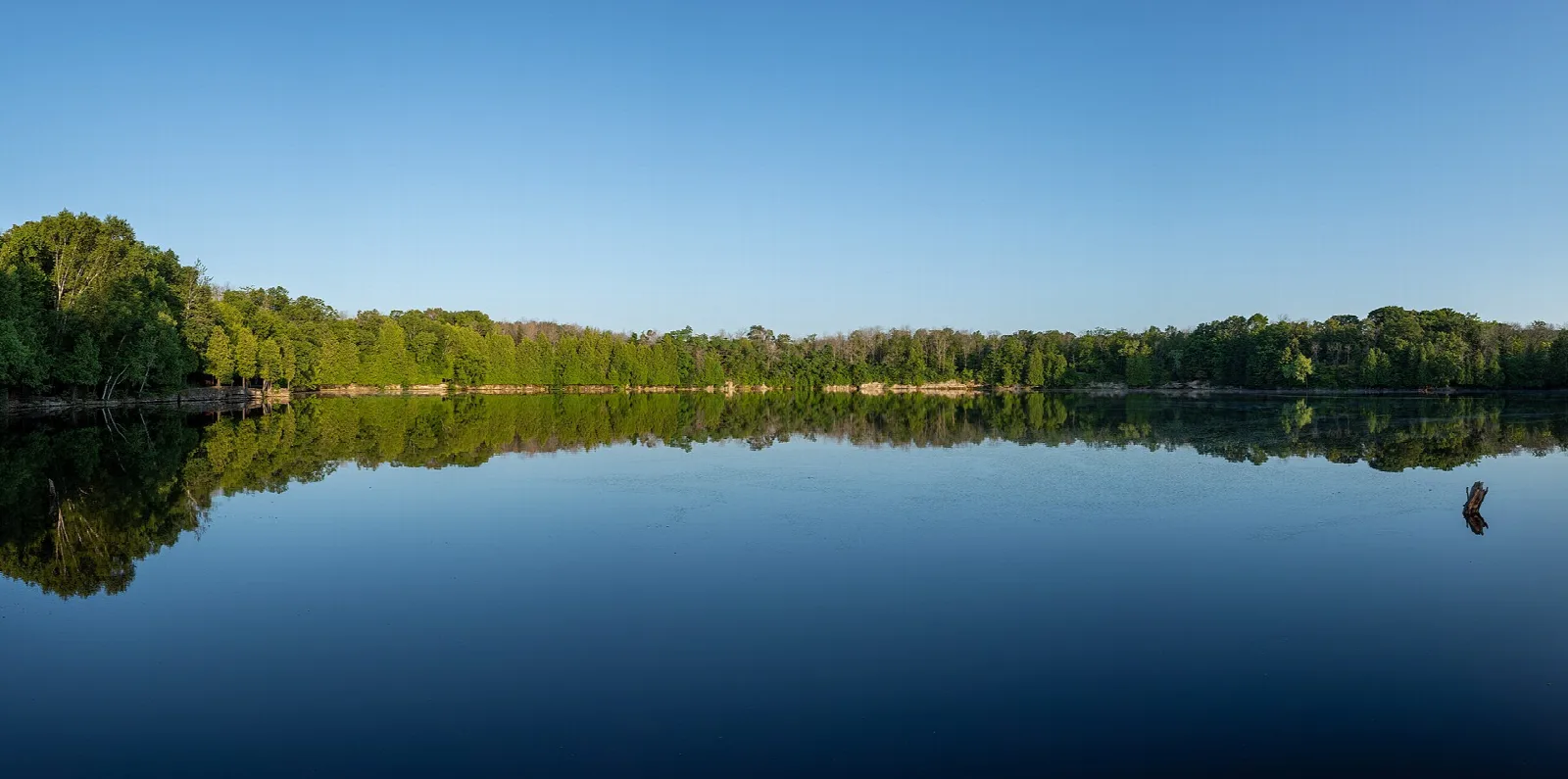 Still quarry lake mirroring a tree-lined shore under clear sky