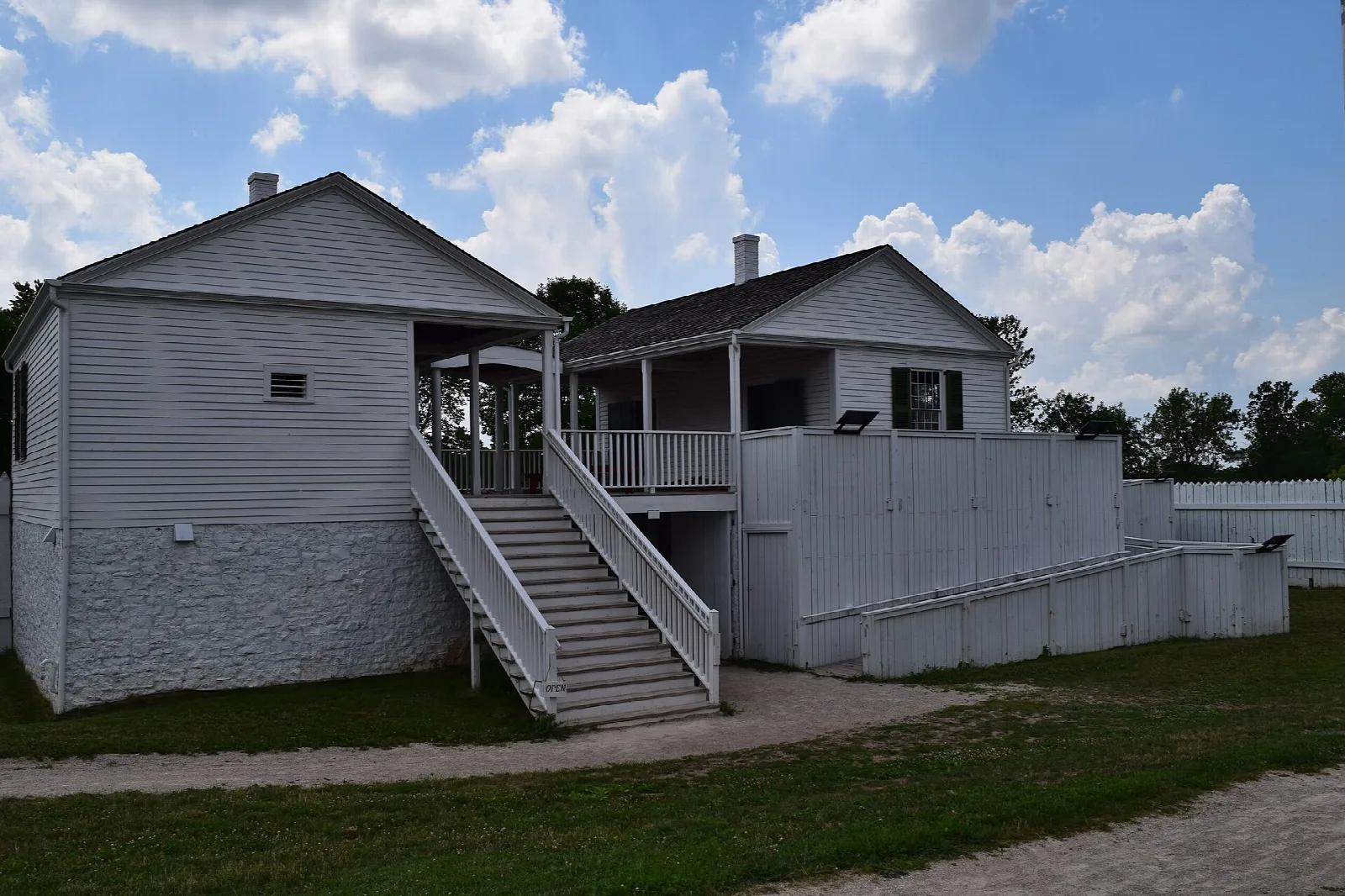 White wooden building with a raised porch and stairs on a green lawn