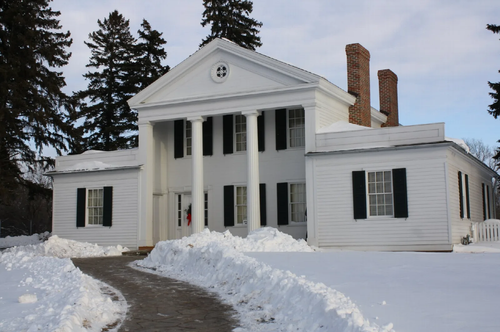 White two-story house with columns and chimneys beside a snowy path