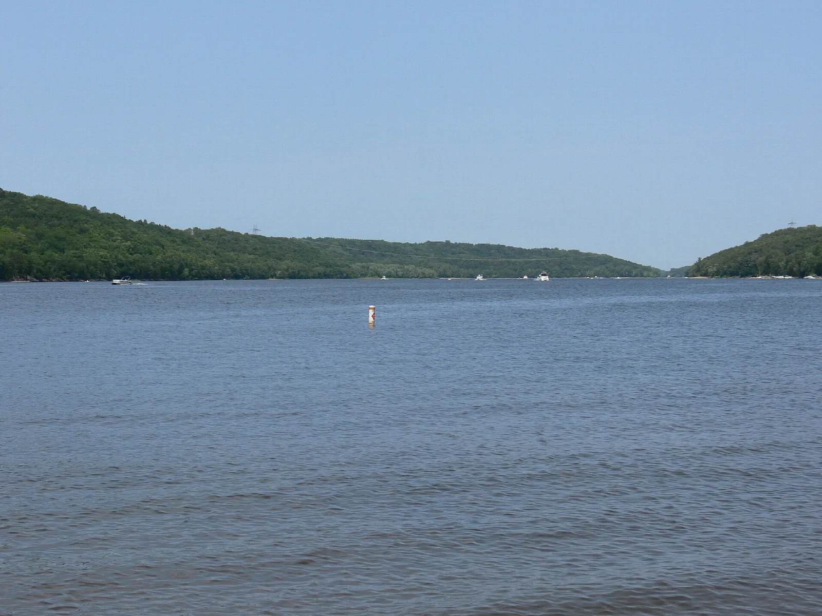 Broad calm river with a tree-covered bluff and a buoy