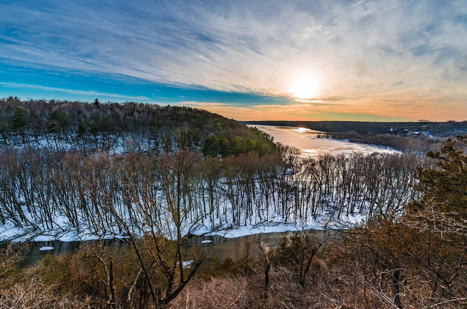 Winter sunset over a river mouth with snowy bare trees in front