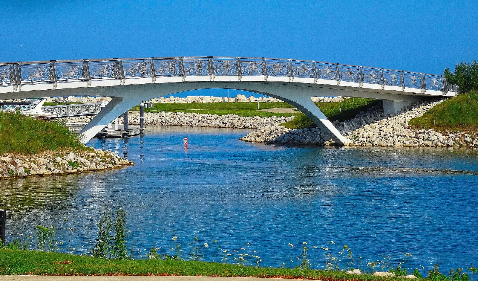 White arched footbridge over a channel with rocks and grass on the banks