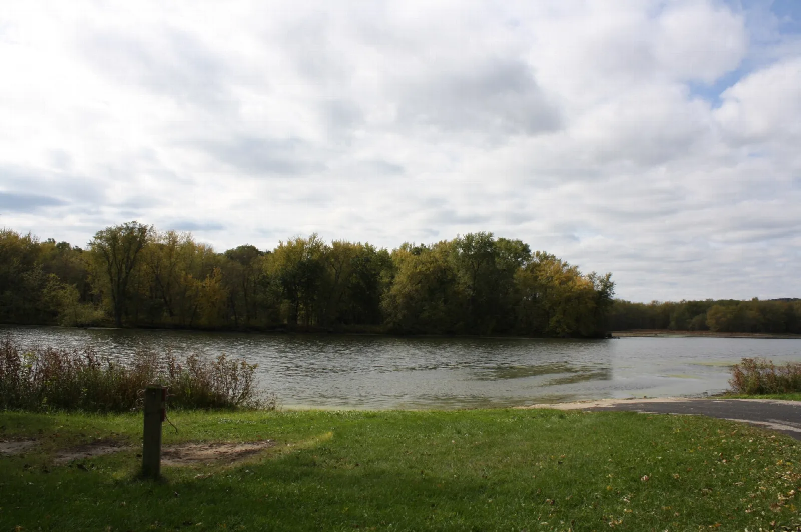 Calm river with a tree line under cloudy sky and a grassy bank