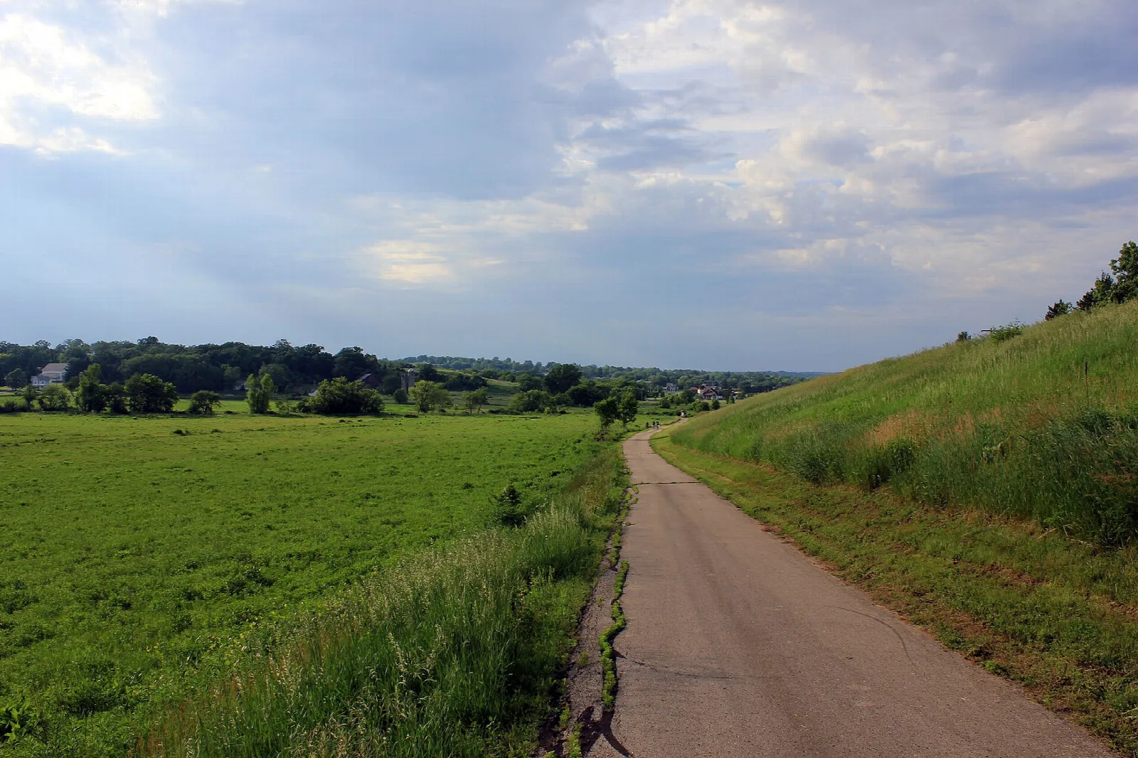 Grassy gravel trail beside a hillside in green fields