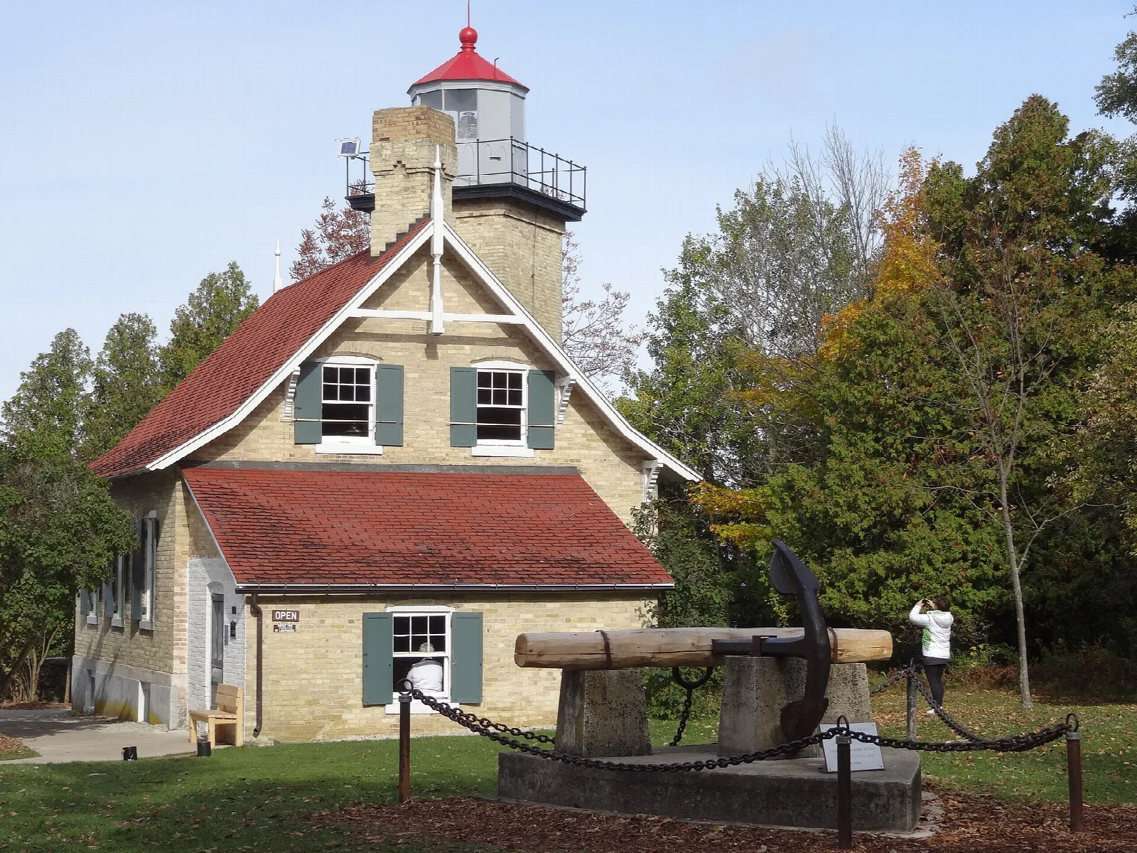 Cream brick lighthouse with a red roof and an old anchor on the lawn