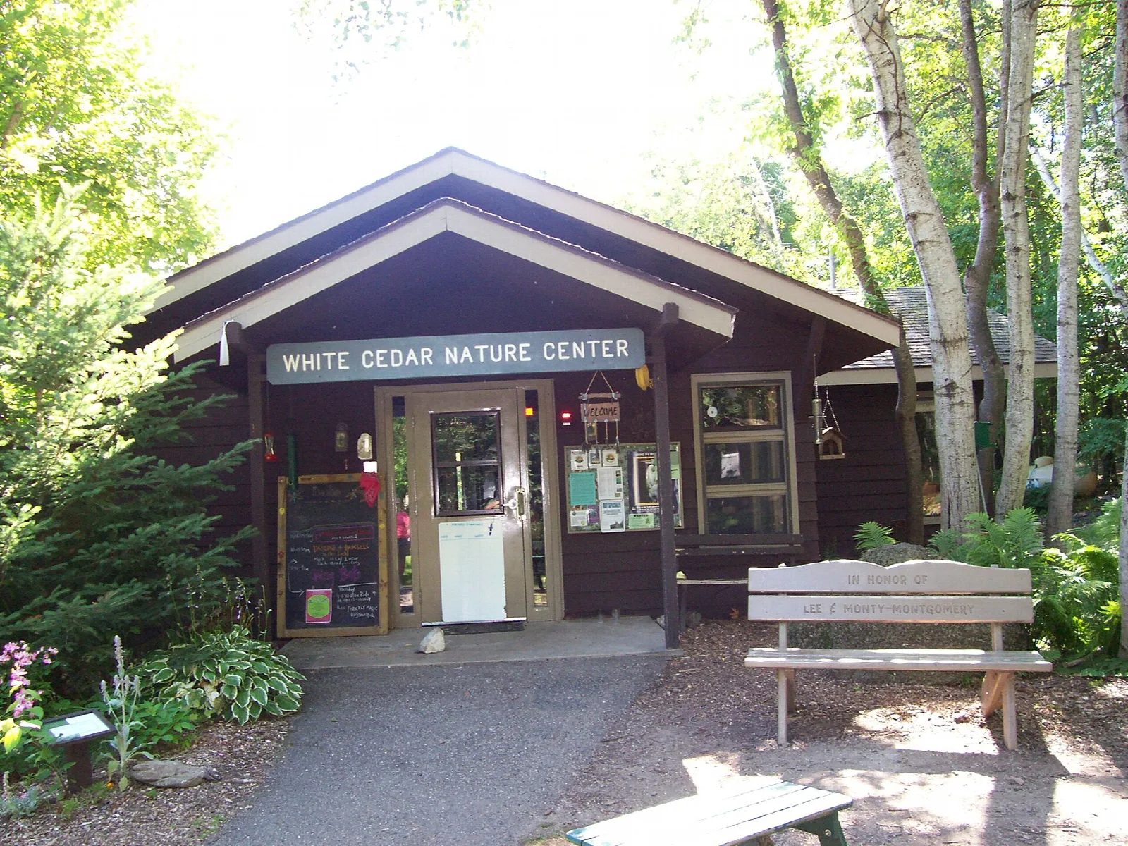 Small brown log building with a White Cedar Nature Center sign and a bench