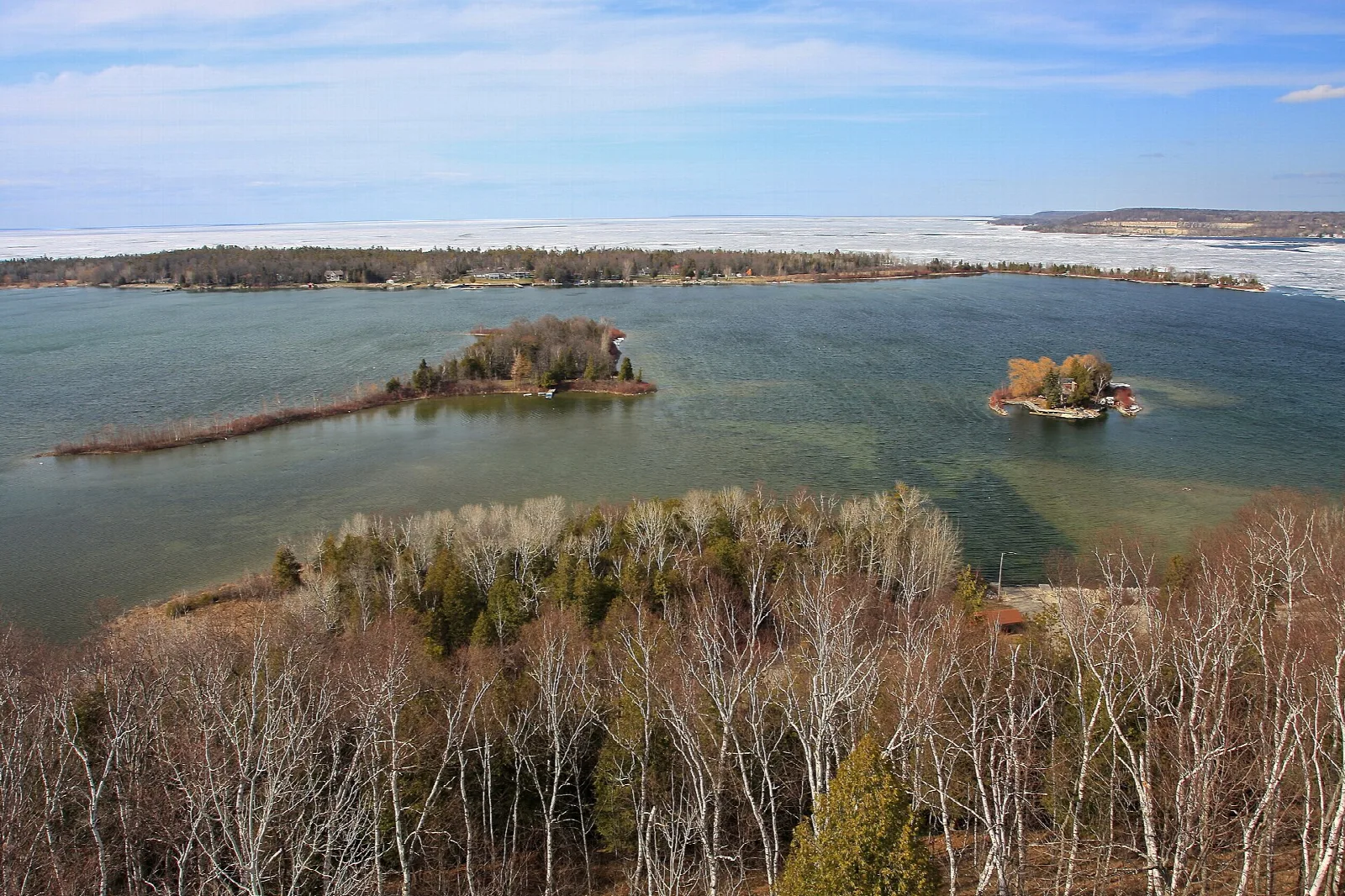 Bay with two small wooded islands seen from above, with bare trees in the foreground