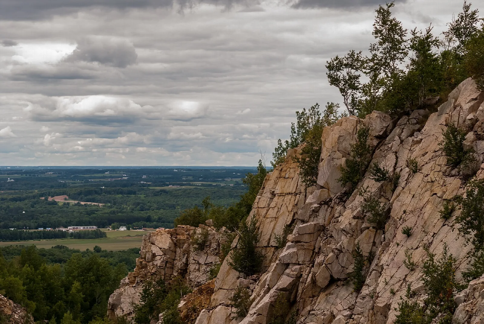 Steep pale rock face with trees on top and a cloudy sky