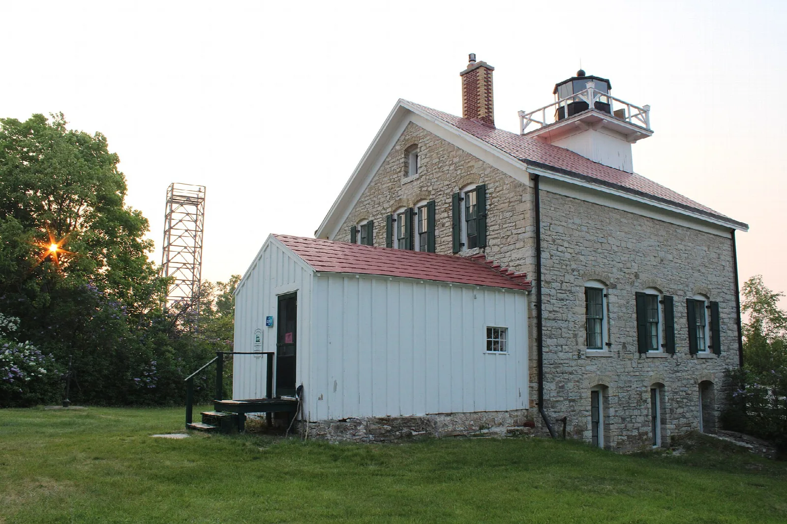 Stone lighthouse with a red roof and white addition beside a lawn