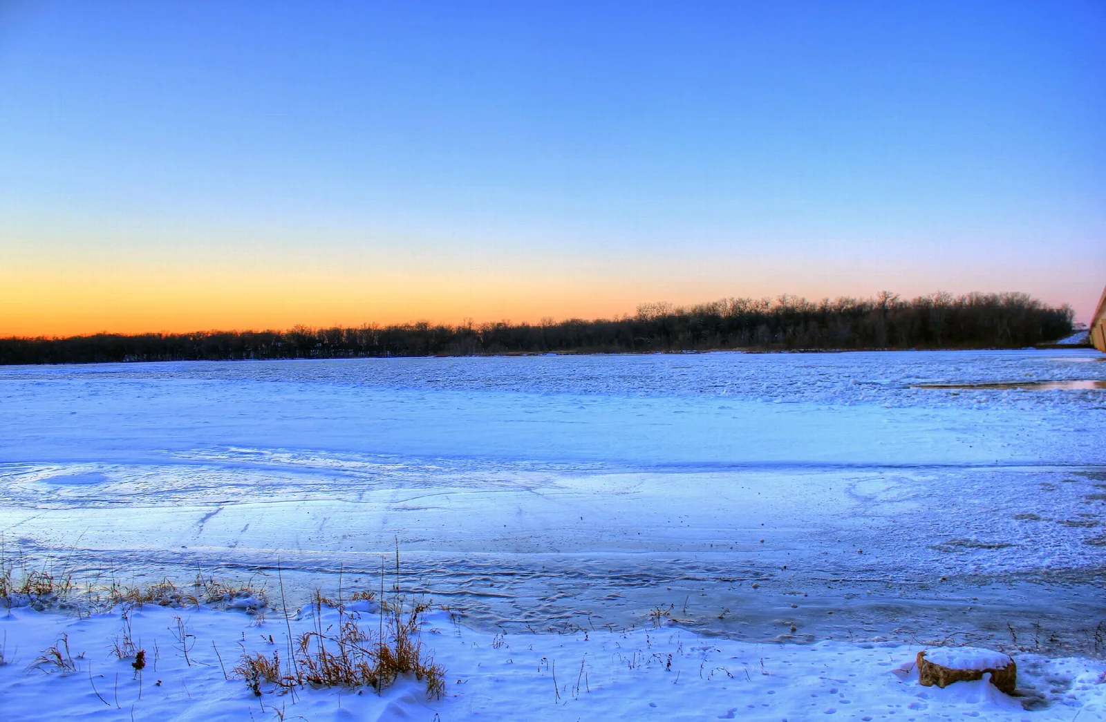 Snow-covered field and trees under an orange horizon glow