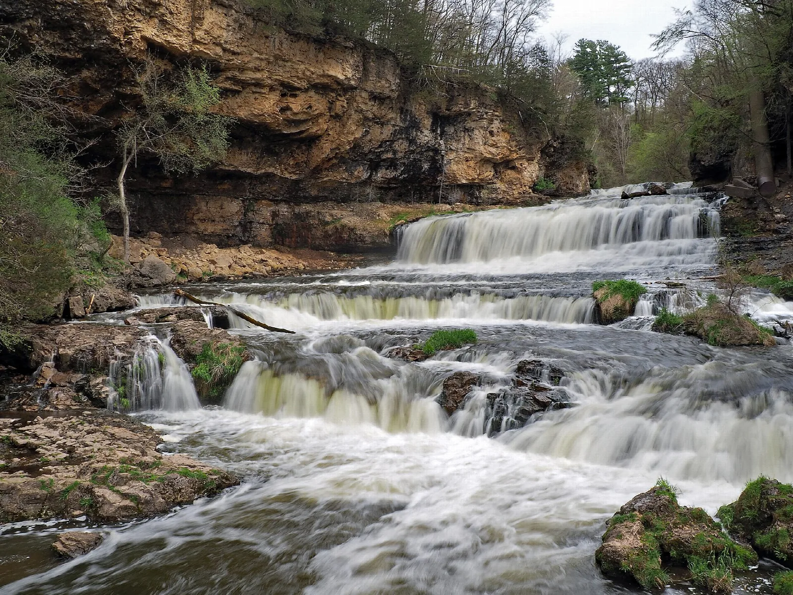 Wide stepped waterfall over a rock ledge below a sandstone bluff