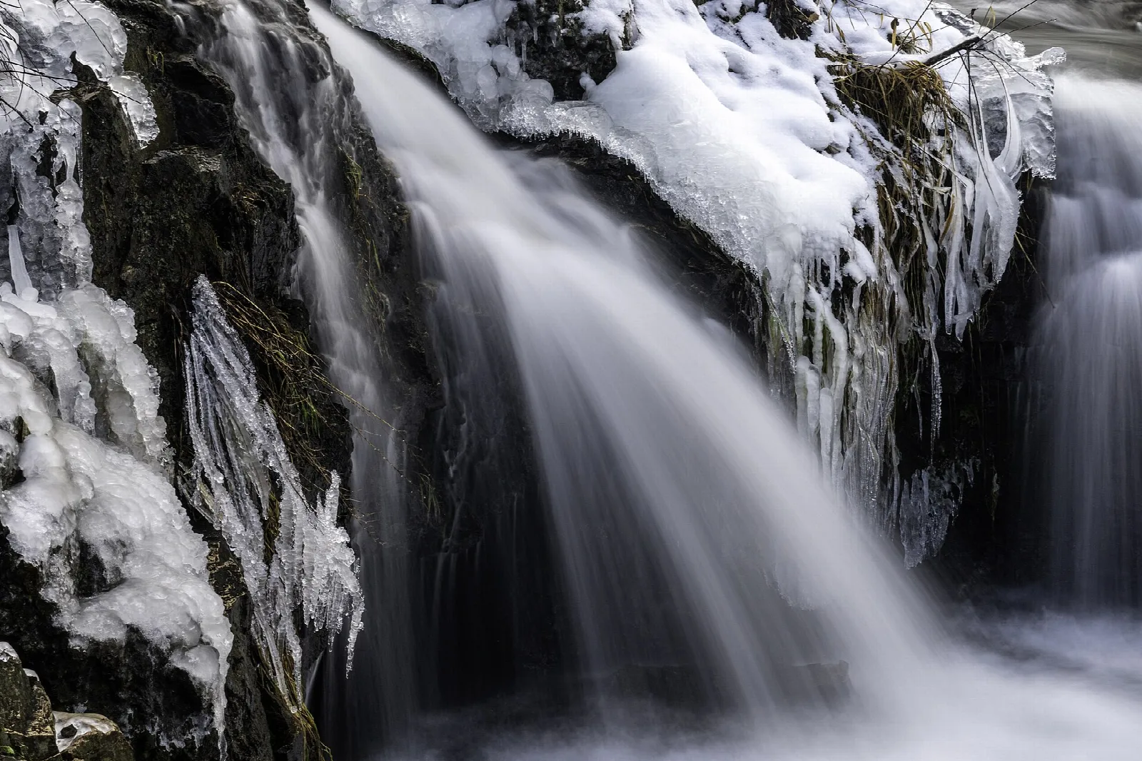 Waterfall flowing over dark rock with ice and snow