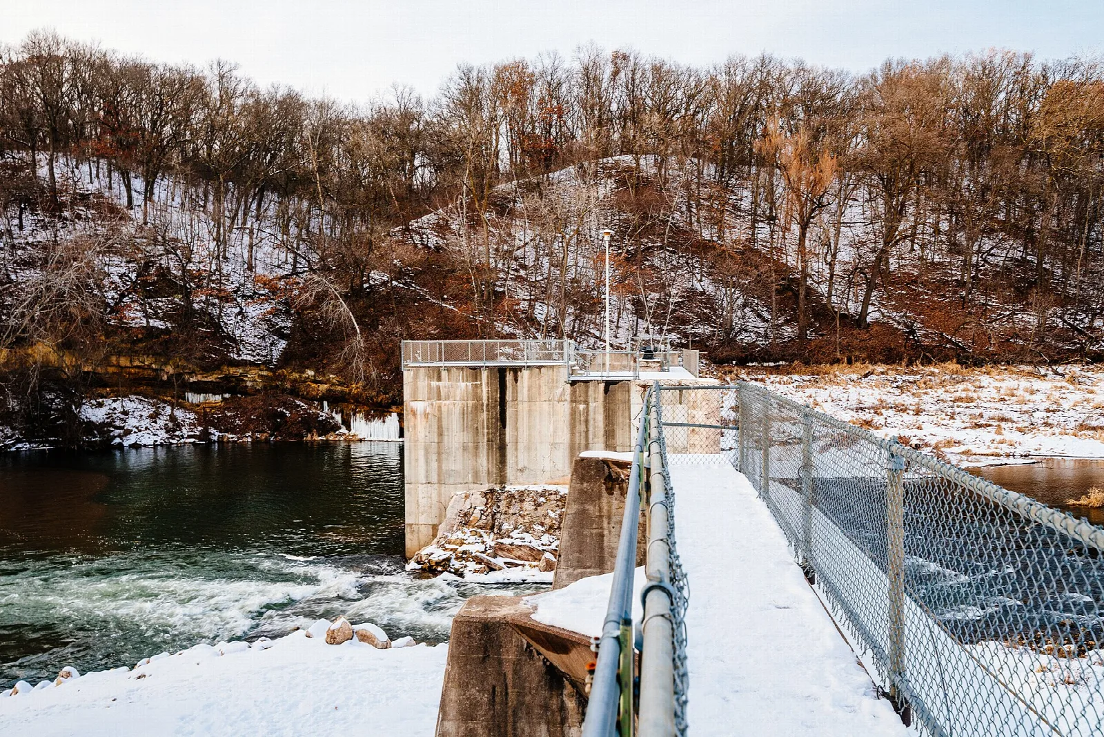 Concrete dam with a fence above a river, snow on the ground