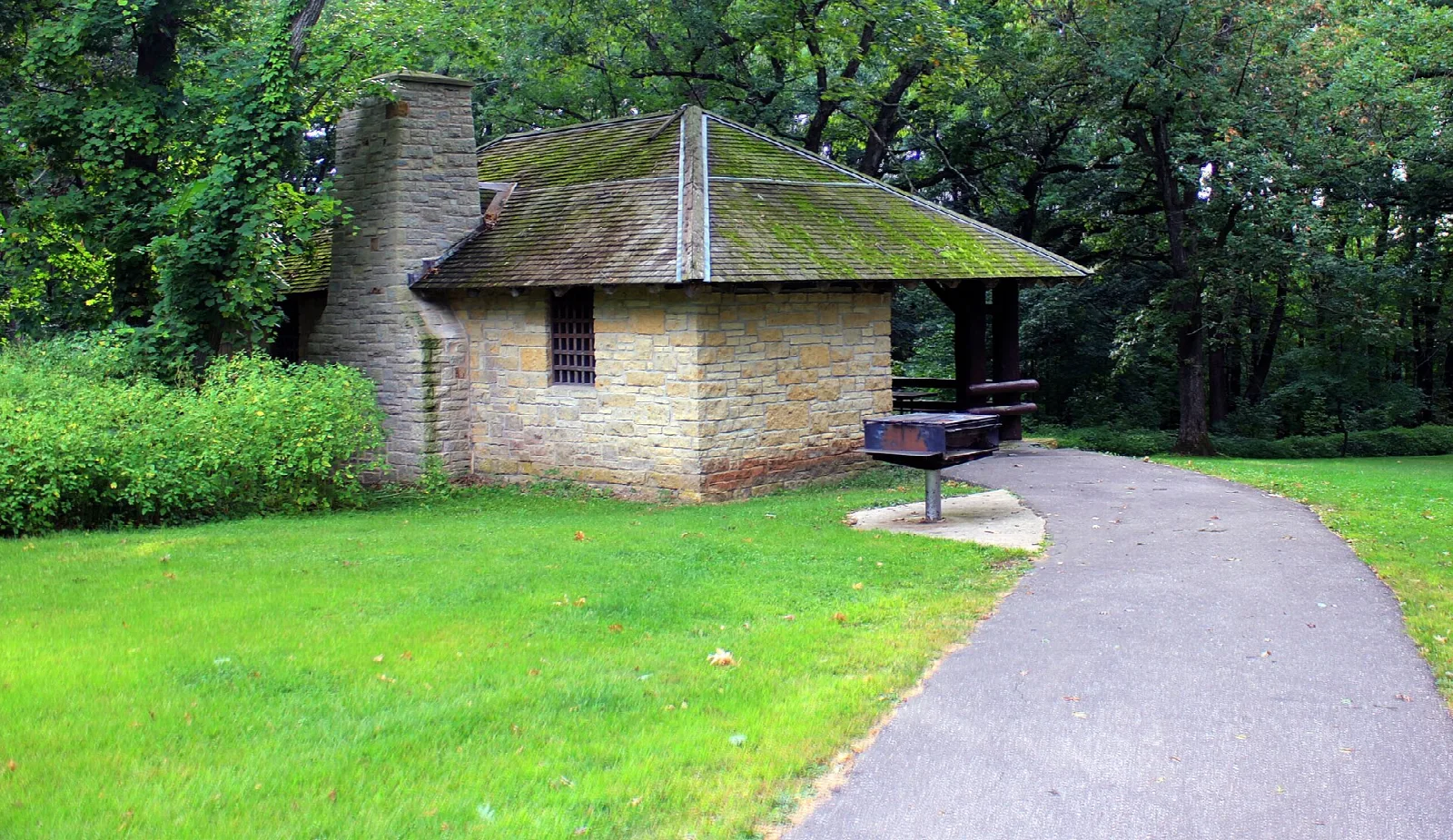Small stone shelter with a chimney beside a paved path
