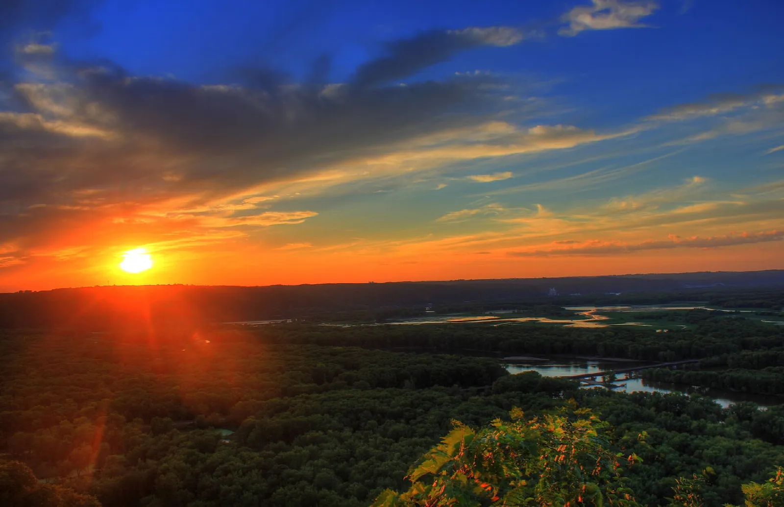 Orange sun setting over forested river bottomland
