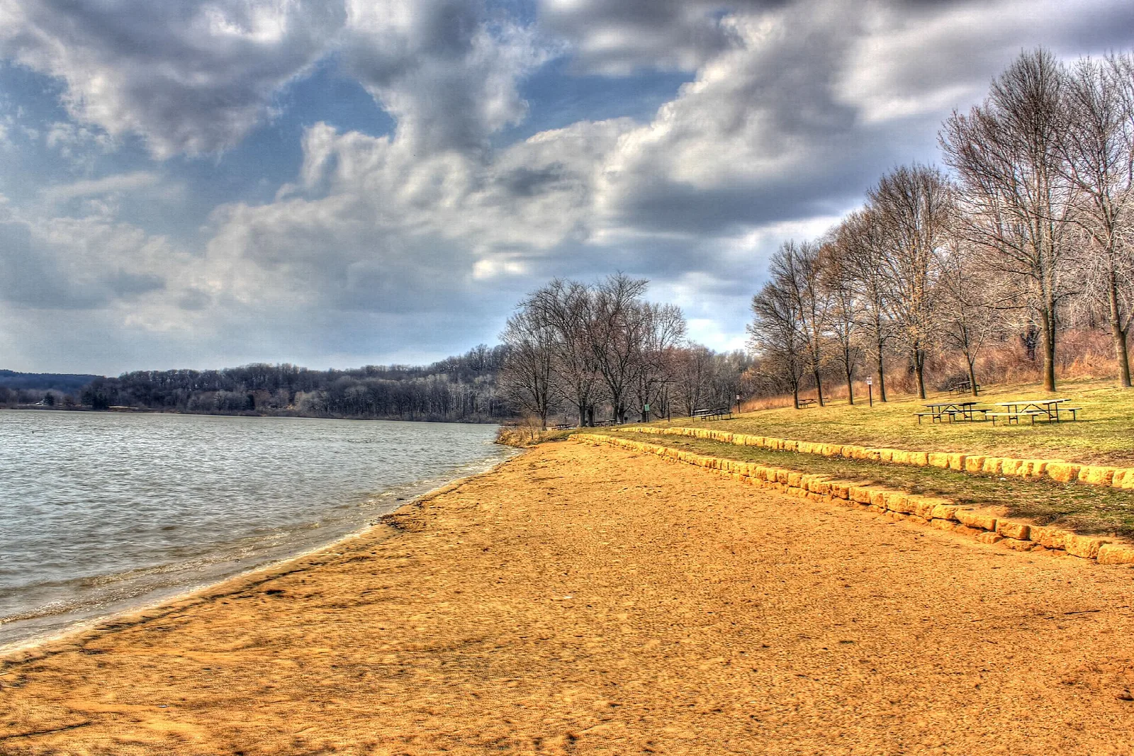 Sandy shoreline curving along a wide lake under a cloudy sky
