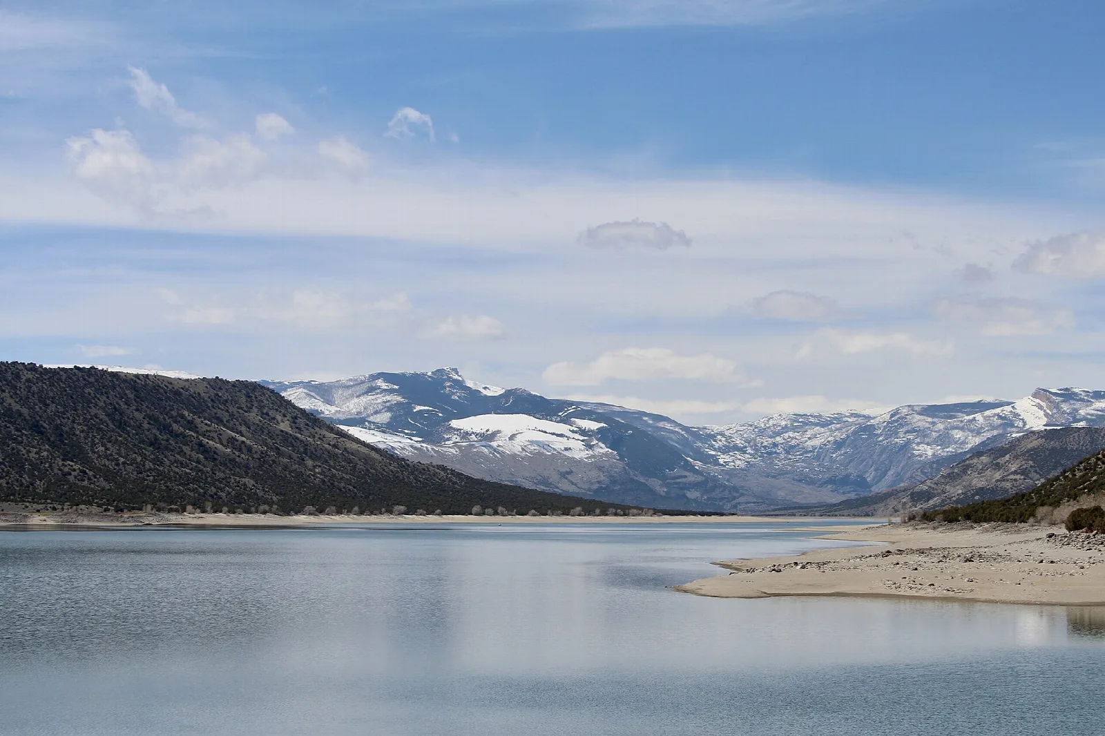 Calm reservoir below dry hills with snowy mountains far off