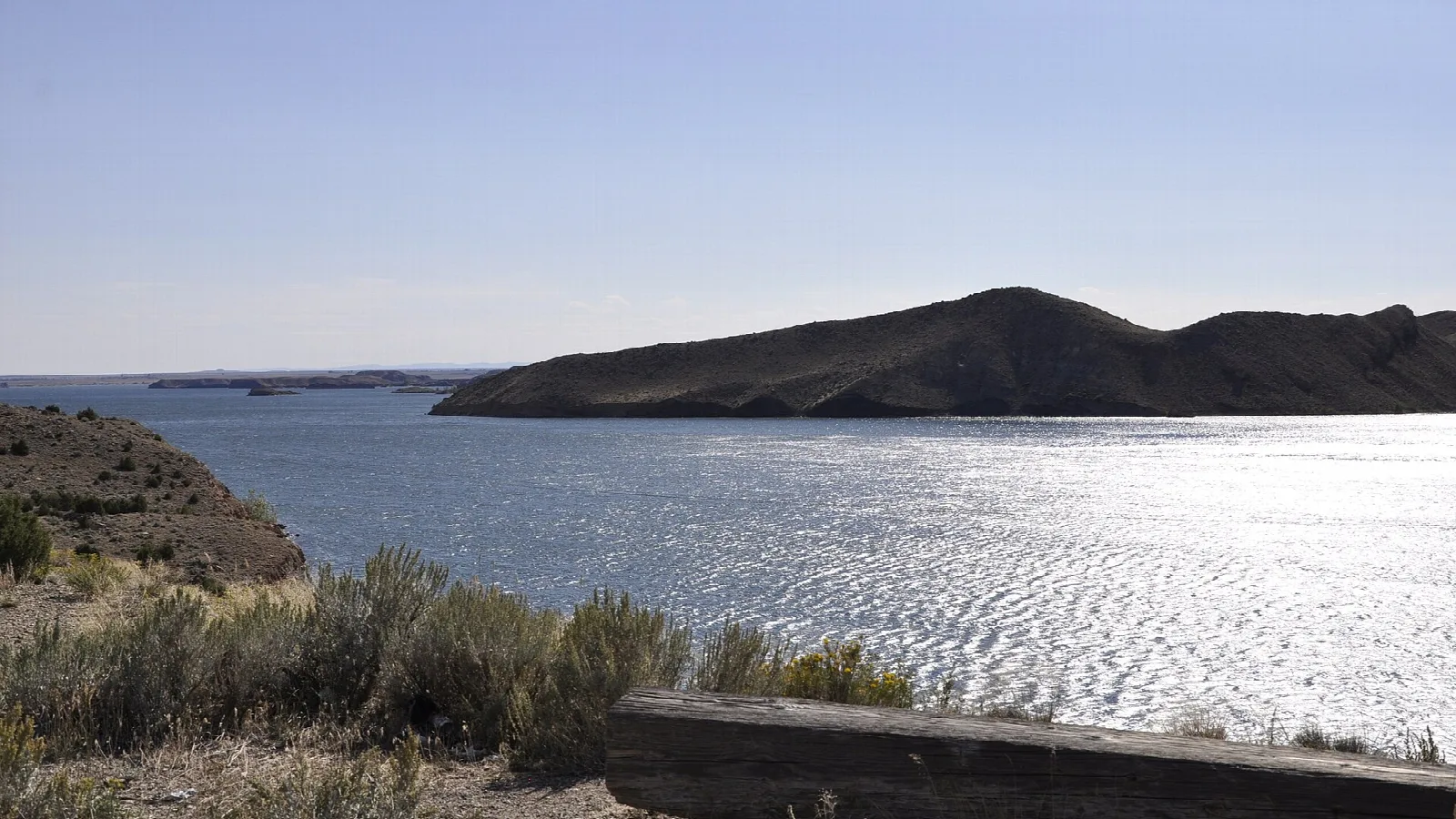 Sunlit reservoir with a dark hill across the water and sagebrush in front