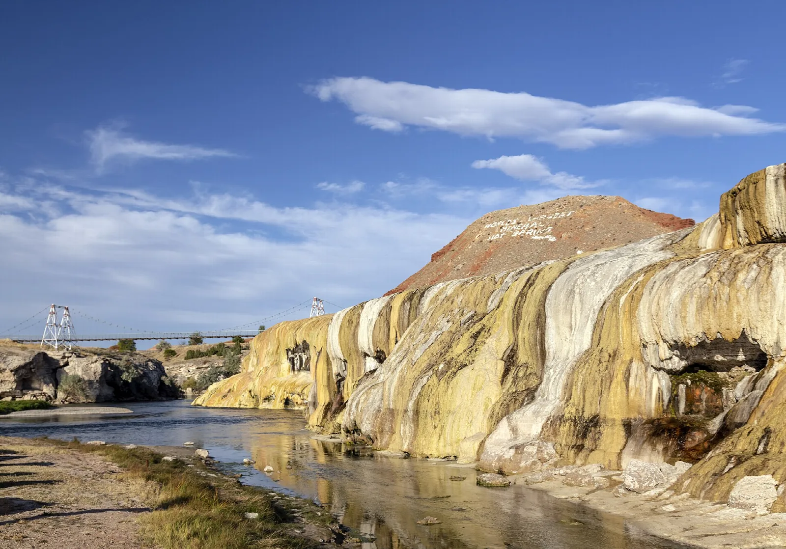 Stream running past a large travertine formation under blue sky