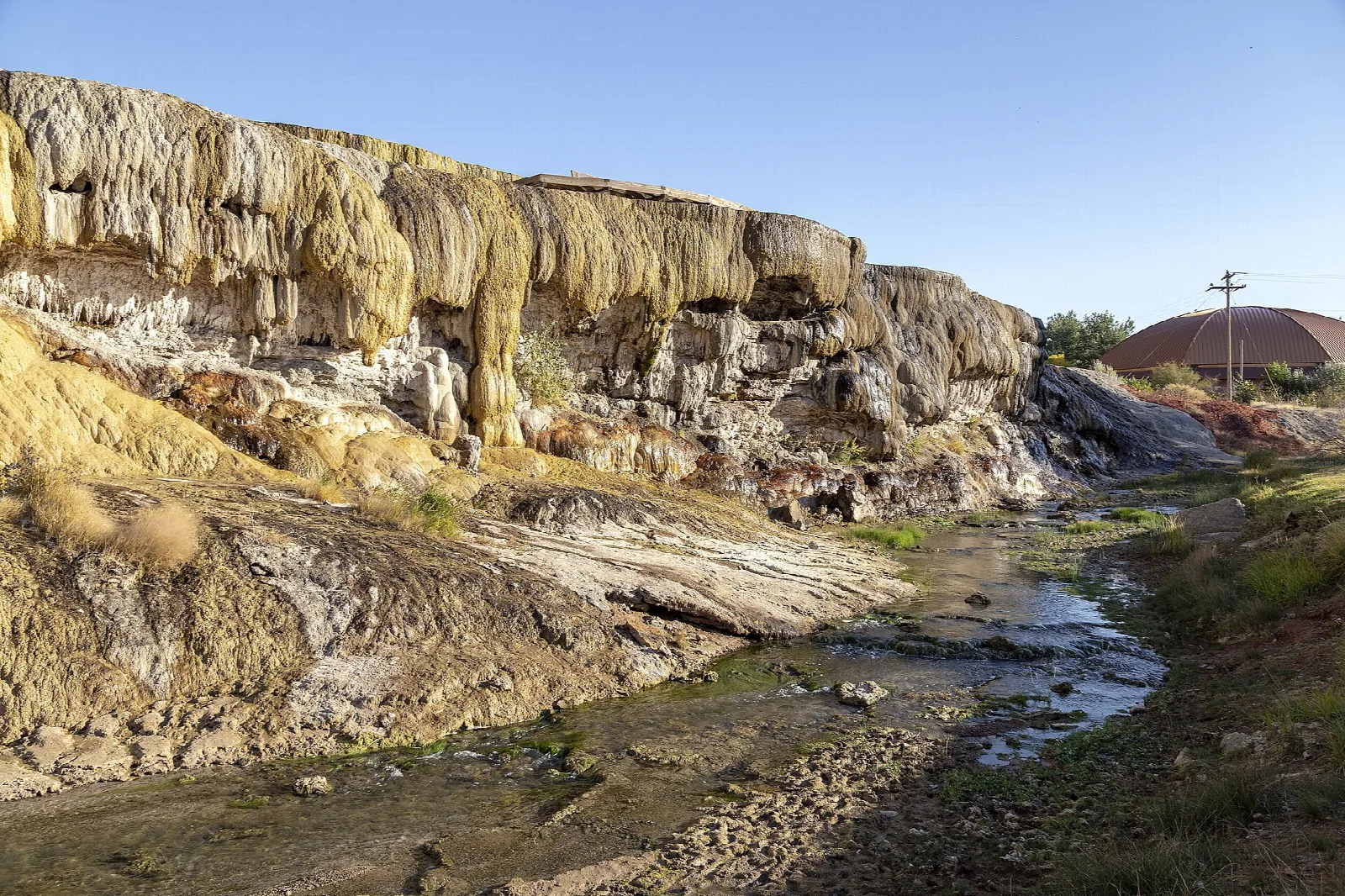 Layered yellow and white travertine terraces beside a small stream