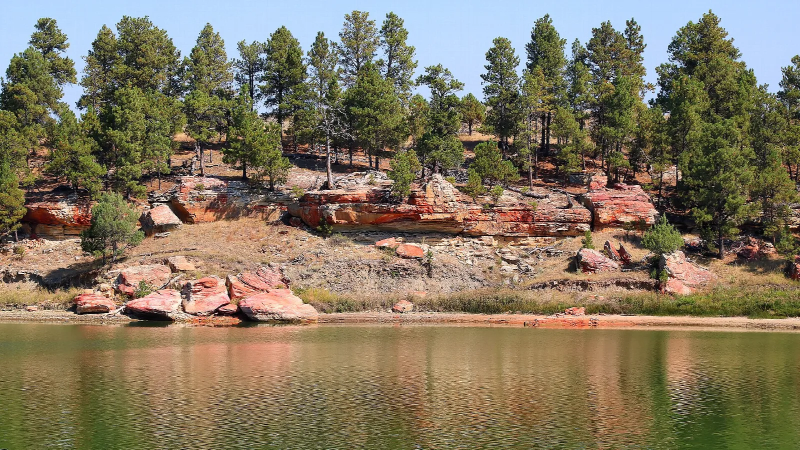 Green lake below red rock and pine trees