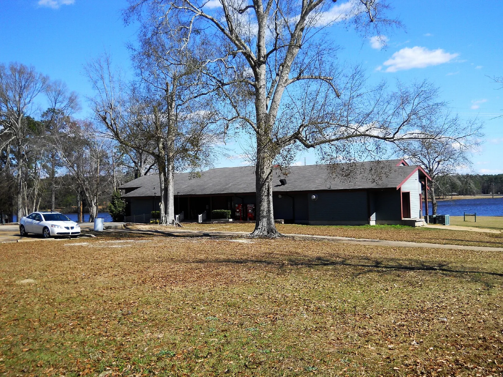 Low building with a parking area under bare trees, lake behind