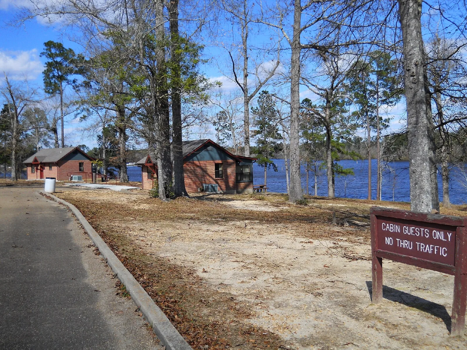 Brick cabins beside a lake with a road and sign in front
