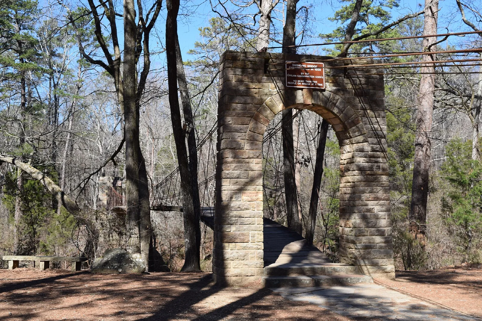 Stone tower of a suspension bridge beside a dirt path in the woods