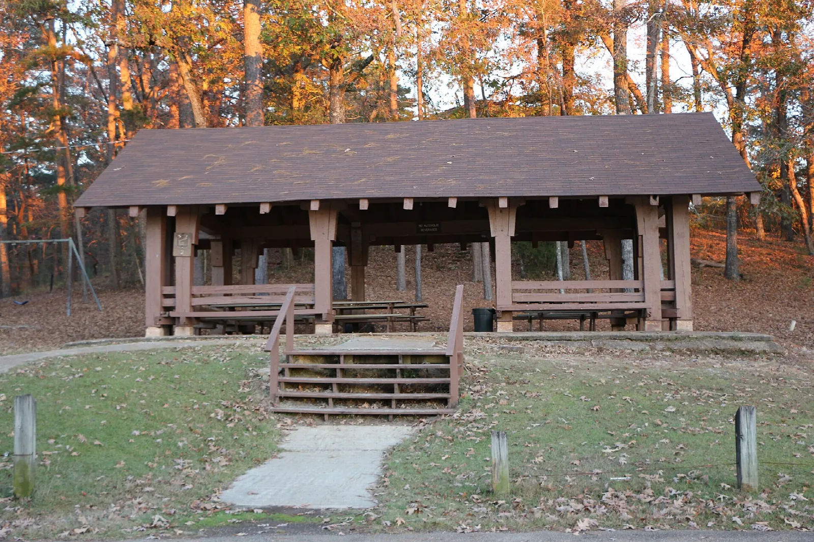 Open picnic pavilion with benches on a grassy slope among autumn trees