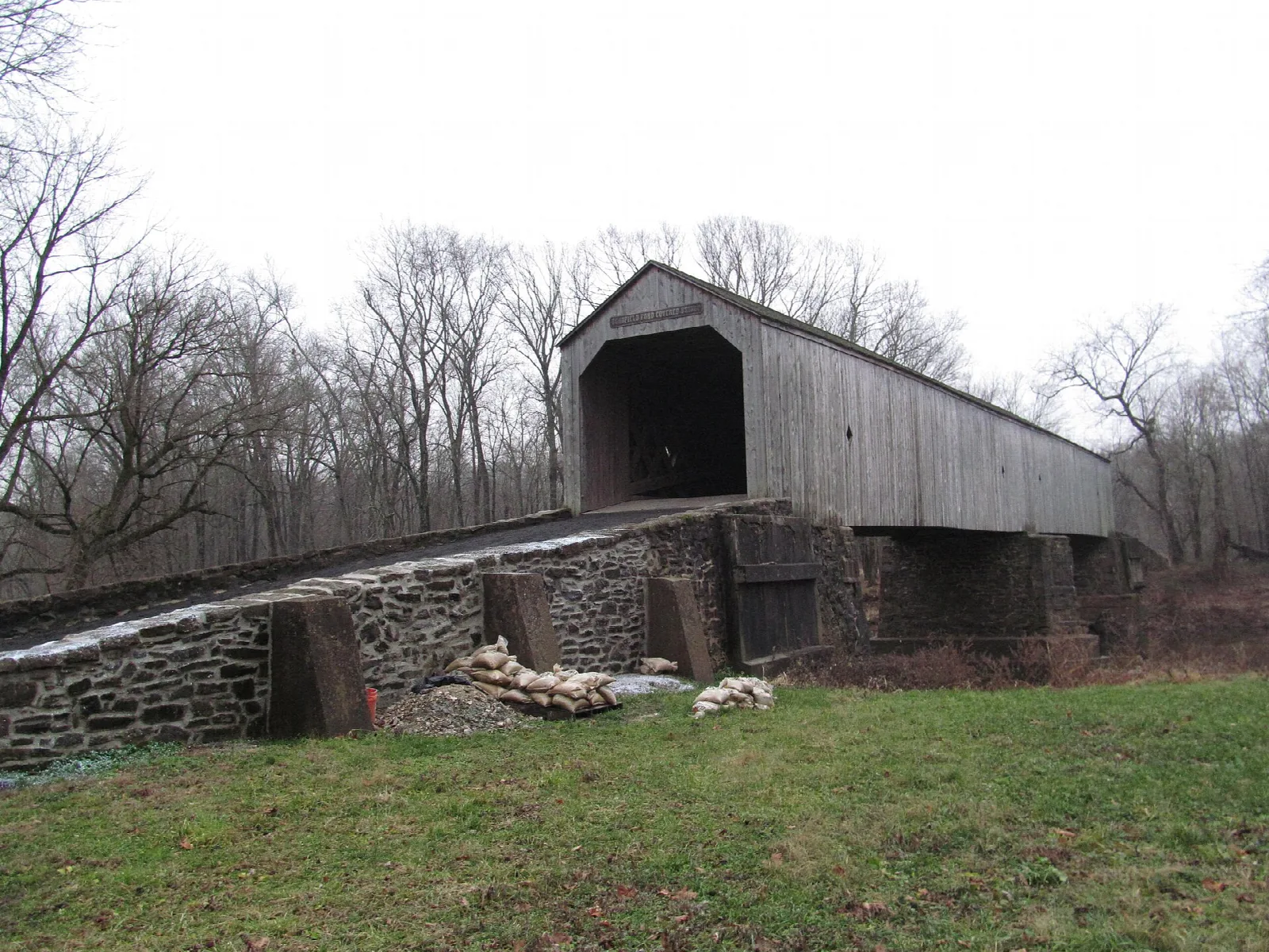 Gray wooden covered bridge on a stone approach beside a green lawn