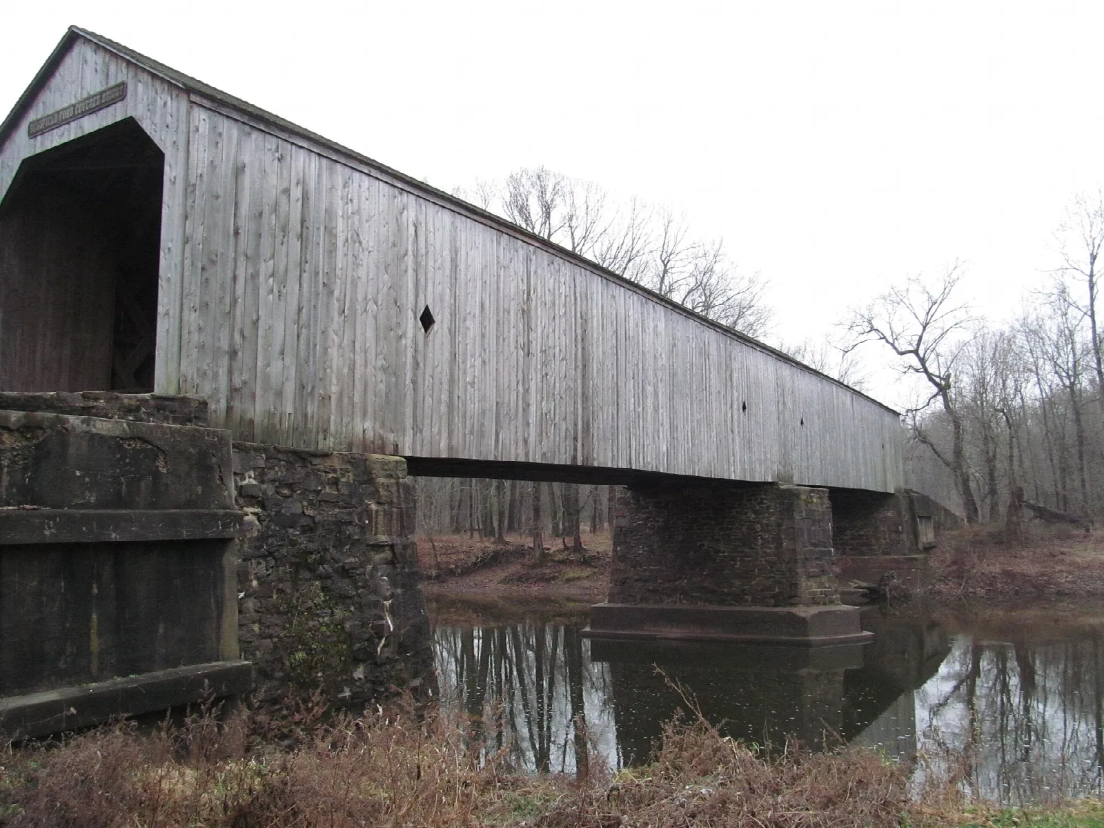 Long gray covered bridge on stone piers over the creek