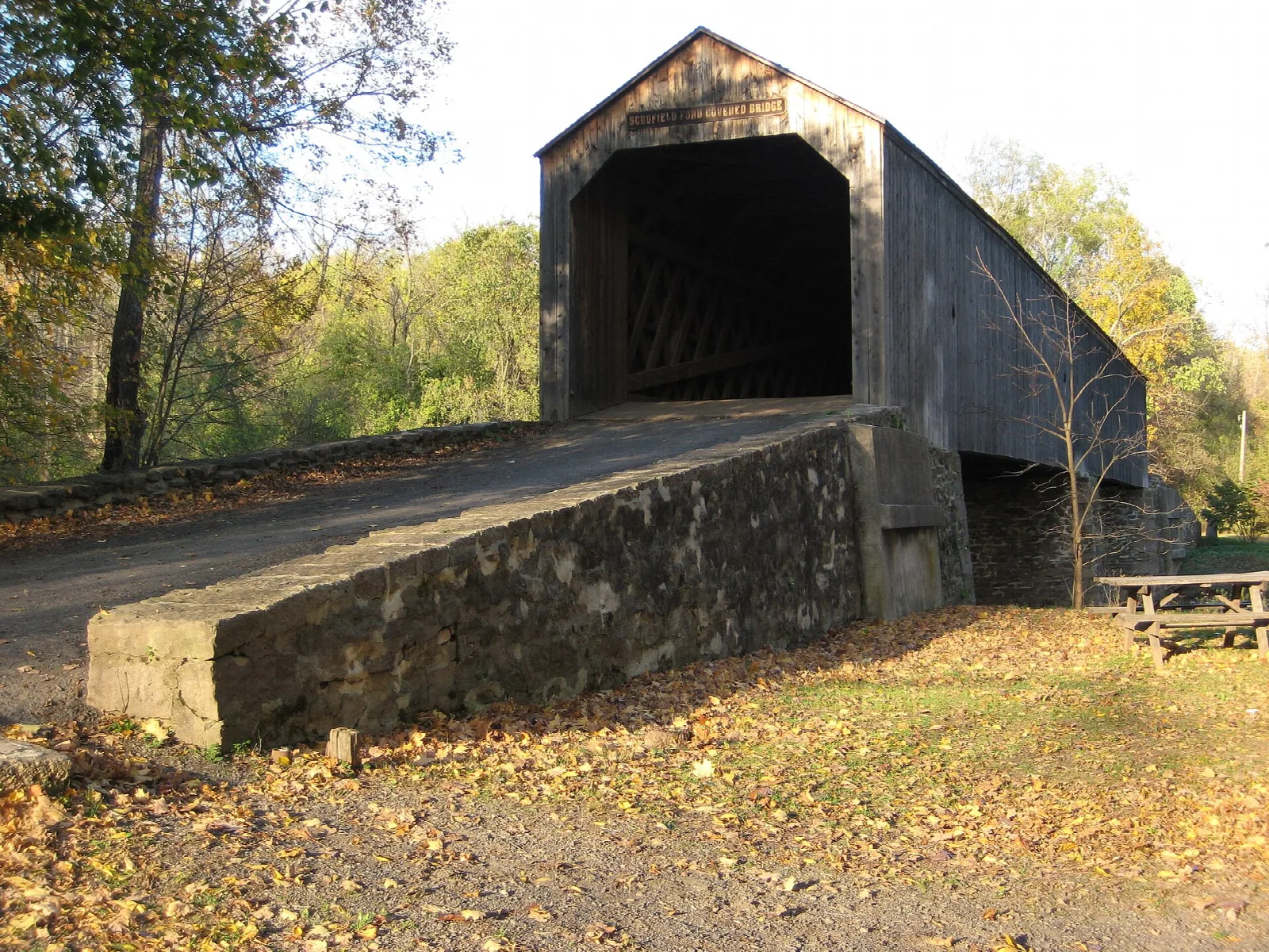 Covered bridge entrance beside a stone ramp and fall trees
