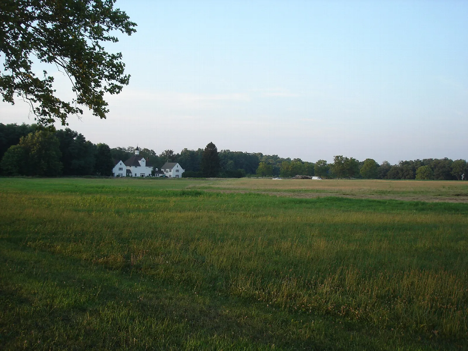 Open mown field with a white farm building and trees in the distance