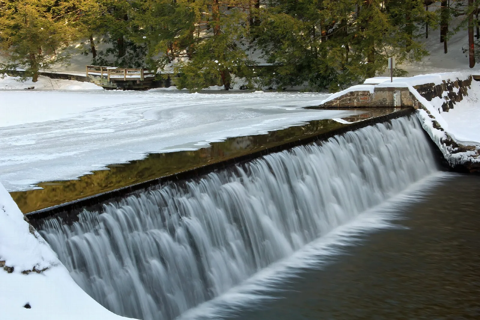 Snow-covered stone dam with water spilling over